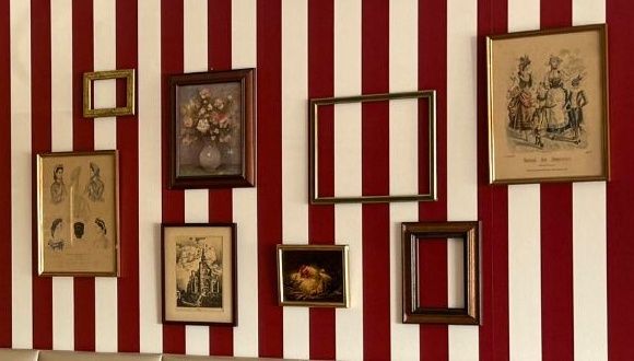 Mur rayé rouge et blanc garni de cadres anciens et de gravures.